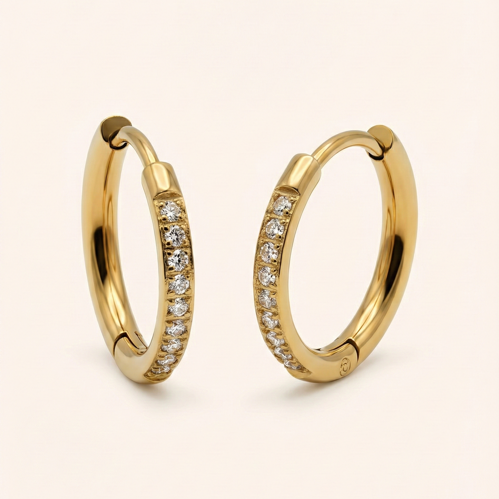Gold hoop earrings with embedded diamonds on a beige background